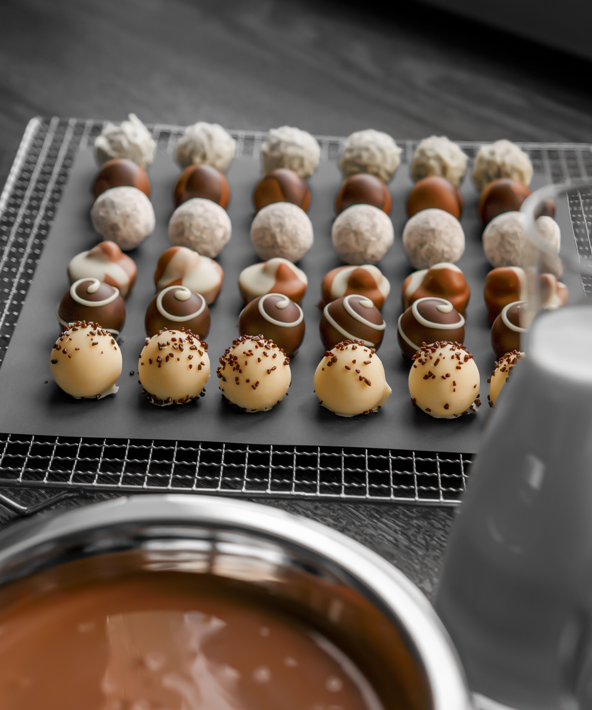 Handgemachte Pralinen liegen auf einem Tablett und davor steht eine Schüssel mit flüssiger Schokolade